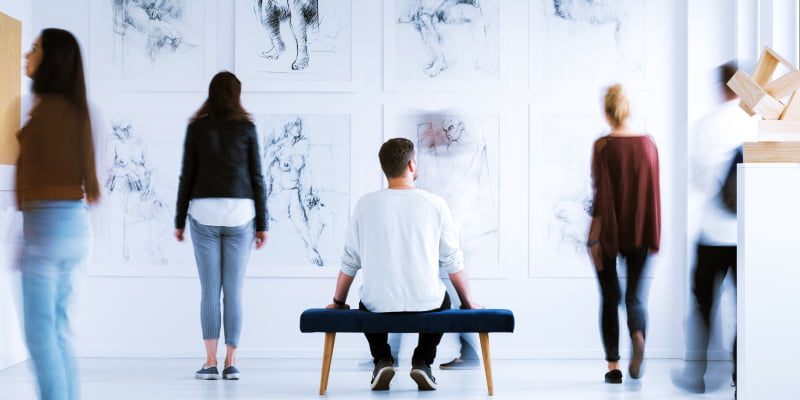 Mann auf Sitzbank schaut sich Gemälde in einer Galerie an